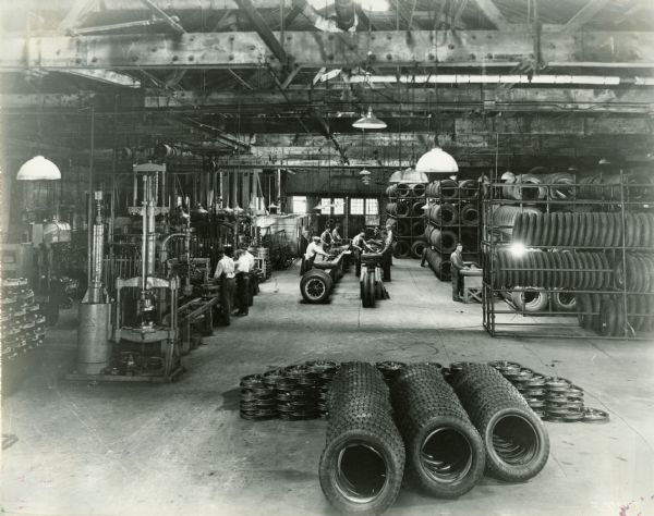 Factory workers assembling pneumatic (rubber) truck tires at International Harvester's Springfield Works. There is a pile of rubber tires and metal rims in the foreground.