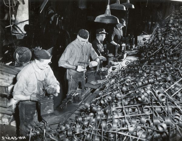 A line of factory workers next to a large pile of metal parts at International Harvester's Rock Falls Works.