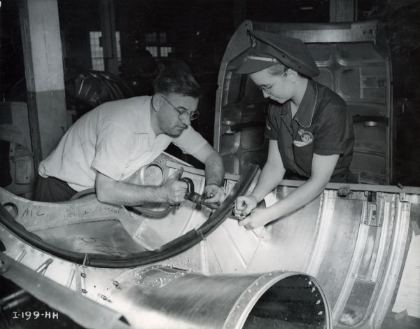 Male and female factory workers make an engine cowling for a Curtiss-Wright C-46 commando cargo plane at Auburn Works.
