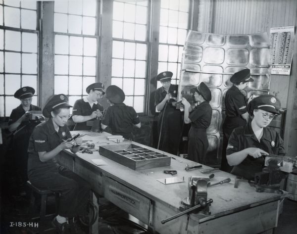 Female factory workers make parts for engine cowlings at International Harvester's Auburn Works. The cowlings were for Curtiss-Wright C-46 Commando cargo planes.