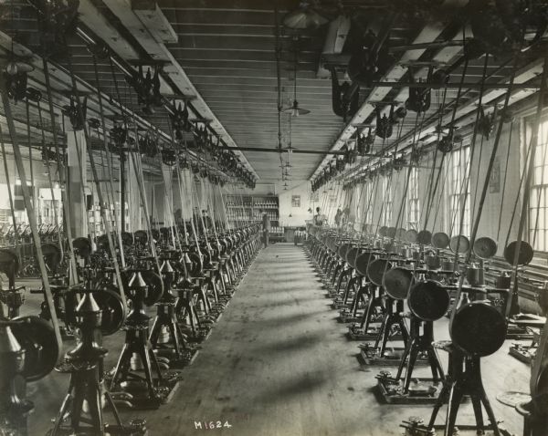 Factory workers manufacturing cream separators at International Harvester's Milwaukee Works. The poster at the back of the room reads: "Dairymade" while the poster on the room's right wall advertises cream separators.
