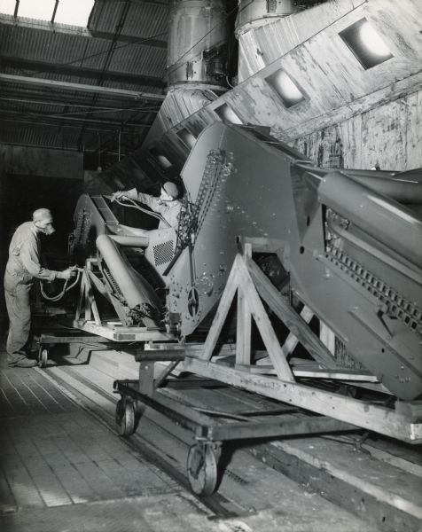 Factory workers paint completed corn picker units at Chatham Works as they pass through a down-draft spray booth on a power conveyor. Over-spray is exhausted through grating in the floor and washed out of the air as it passes through stacks in the rear.
