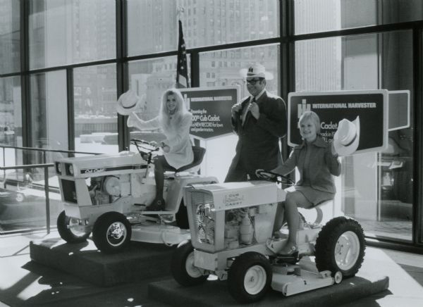 The original caption reads: "Comely Chicago models Dianne Trunda (left) and Joyce Szulc (right) help Earl A. Comerford, manager, agricultural and consumer products, International Harvester Company, celebrate completion of 500,000th lawn and garden tractor.  IH began manufacture of lawn and garden equipment in 1961 and now is fast in the production of a complete line of lawn and garden equipment for home and commercial use." The two women are sitting on Cub Cadet lawn tractors.
