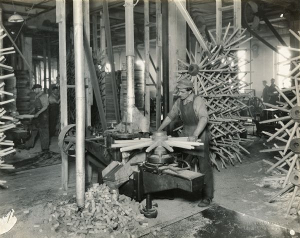 Factory worker cutting spokes for wagon wheels at International Harvester's Weber Wagon Works. Other men are working in the background.