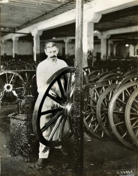 A factory worker applying grease to a wagon wheel at International Harvester's Weber Wagon Works.