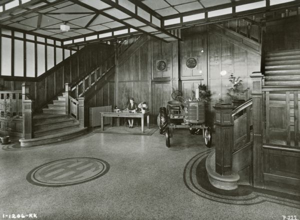 A female receptionist sits at a desk near a Farmall tractor in the entryway of "Harvester House" in Melbourne, Australia. Two large staircases are on the right and left of the receptionist.