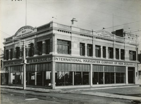 Exterior view of an International Harvester general agency (dealership) building in New Zealand. A sign advertises "British & American Built Farm Machinery."