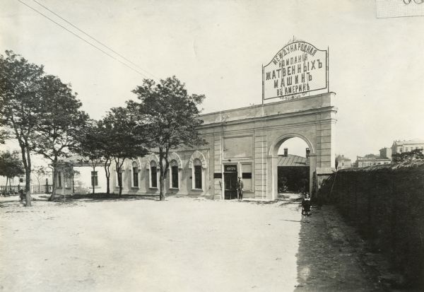 International Harvester's sales office and warehouse at Odessa, Russia.  A young girl in a dress stands near an arch and a man in uniform stands at the entrance.