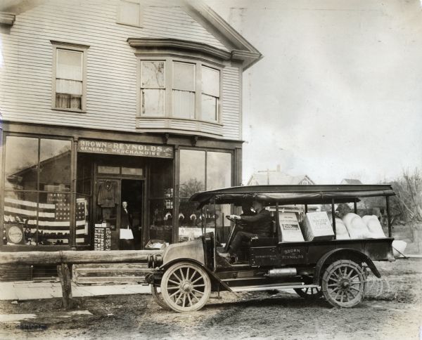 International truck parked outside of the Brown and Reynold General Merchandise store. The truck is loaded with boxes of Post Toasties, Toasted Corn and bags of flour. The store has a large American flag in the window and was possibly located in Springville.