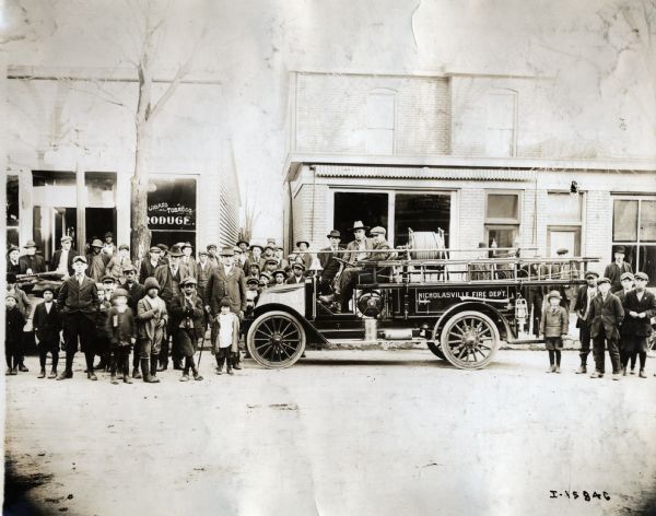 A large crowd of men and boys gathers around an International fire truck parked in street.