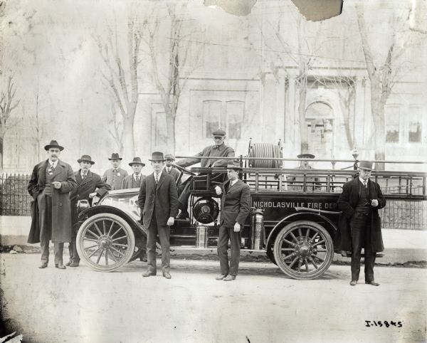 A group of distinguished men in hats, coats and suits are standing around an International fire truck.