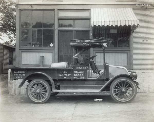 A man sits in an International truck. The truck carries high grade sanitary sodas, presumably from the company of Wm. Williams and the Baltimore Bottling Works.