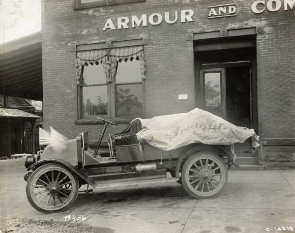 The first International Armour and Company Packing truck outside of the comapny offices. Two American flags are mounted at the front of the truck.