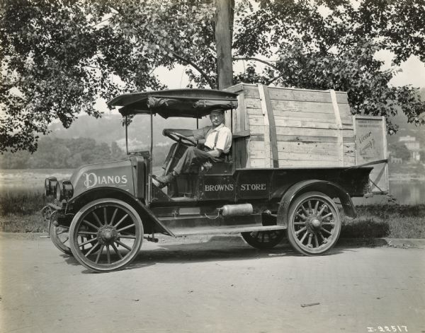 A driver sitting in the cab of an International piano delivery truck for Brown's Store. In the back of the truck are two large wooden crates, one presumably a piano, and the other a Victor Gramophone.