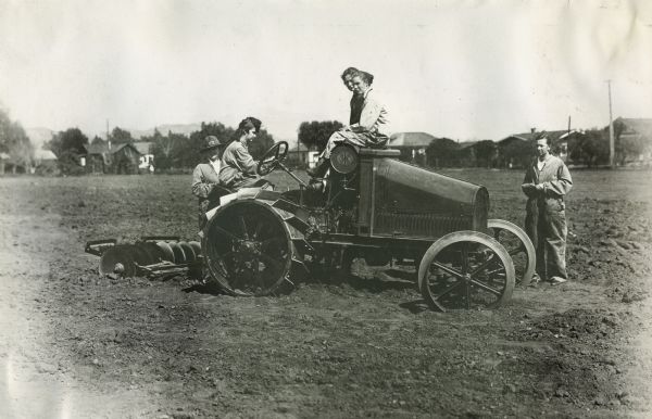 A group of men and women gather on top of an International 8-16 tractor in a field during an educational course on how to operate the tractor.