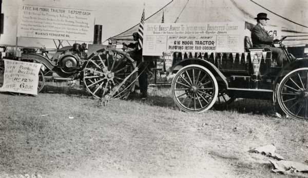 Advertisements and displays for the International Harvester Mogul 8-16 tractor announcing its plowing demonstration inside the "fair grounds". A man is sitting in a truck (International Auto Wagon(?)) decorated with a sign and International Harvester advertising pennants. The event may have been a fair or a tractor show.