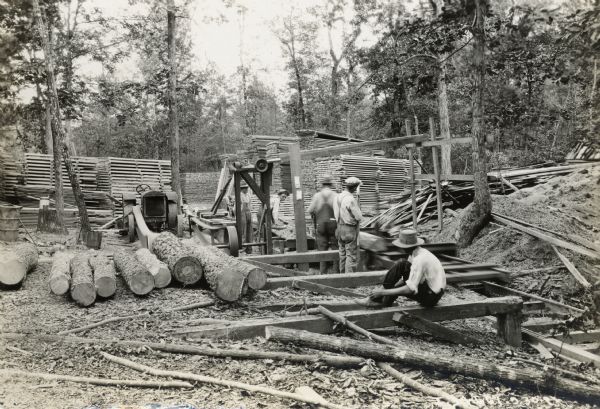 Men cutting logs with a saw powered by a McCormick-Deering 10-20 industrial tractor.