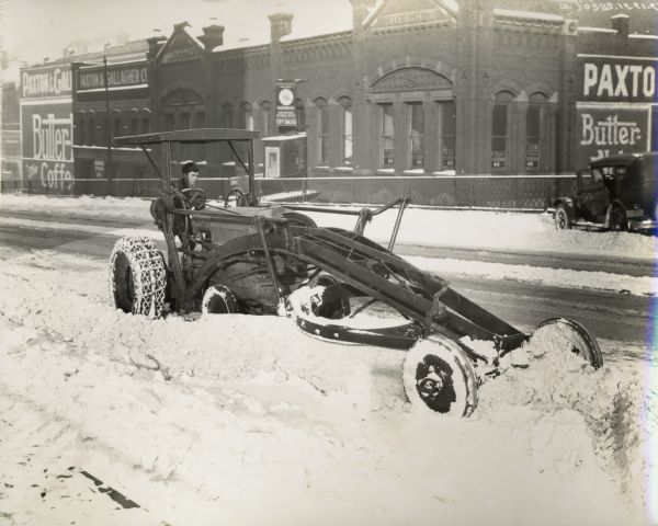 Man plowing a snow-covered city street with a McCormick-Deering 10-20 industrial tractor. A building with the sign "Paxton & Gallagher" is in the background. The photograph was likely taken from the 10th Street bridge in Omaha.