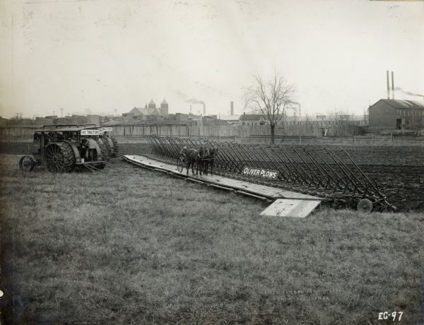 A long row of Oliver Plows hitched to three Mogul 45 tractors. A two-pony cart and driver are parked in front of the plows.