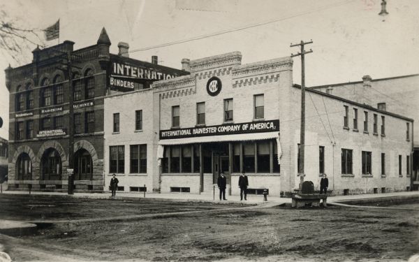 Men stand on a street in front of an International Harvester branch house.