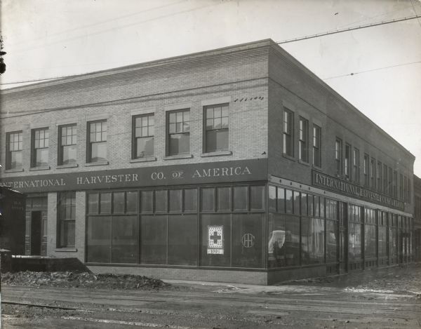 International Harvester branch house. Railroad tracks are near the building. A flag hangs in the window with a small cross shape, stars and "100%" printed on it.