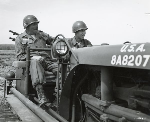 Sergeant Dennis McGhee and a student in an International crawler tractor (TracTracTor) built for the U.S. Army. The student is learning how to operate the crawler. The original caption reads: "Sergeant Dennis McGhee directs students over a four-foot high levee, proves that the big machine does not easily tip."