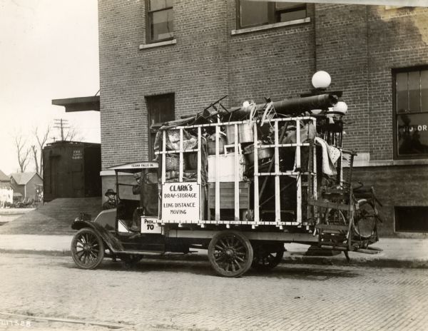 Two men with an International Harvester Model F (or 31) truck piled high with household items. The truck was operated by Clark's Dray-Storage and Long Distance Moving.