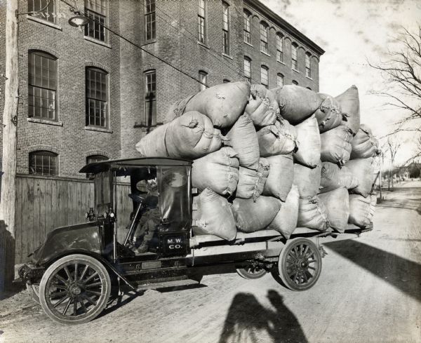 International Model F (or 31) truck with its bed piled high with massive sacks of goods. The photographer's shadow is on the road in front of the truck.