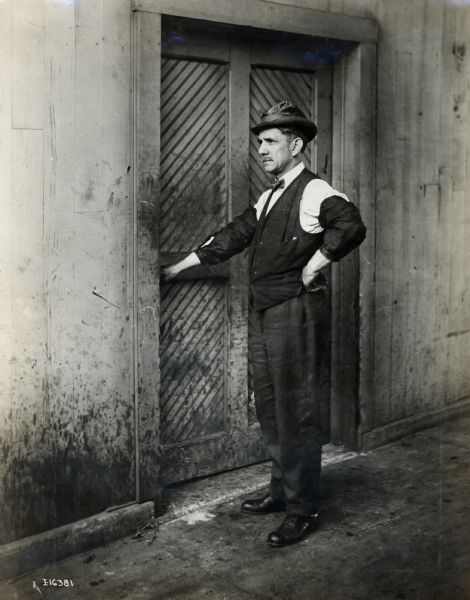 Portrait of a man standing in office clothes just outside a factory door. The man was an employee of International Harvester, likely in Chicago.