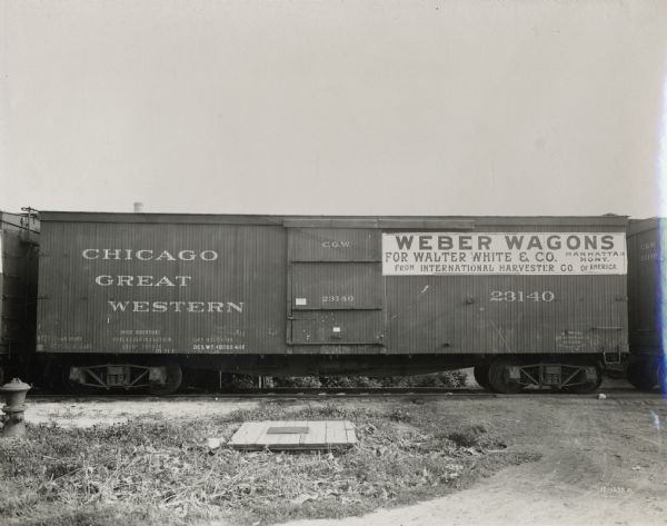 A boxcar in a Chicago Great Western train carrying International Harvester Weber wagons. A sign on the car indicates that the wagons are bound for Walter White and Company in Manhattan, Montana.