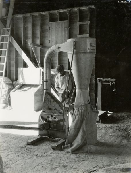 A man works with an International Harvester No. 1 Hammer Mill in a large wooden barn.
