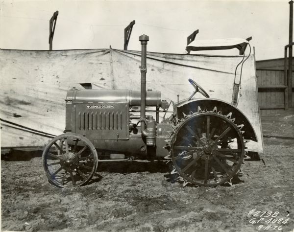 Engineering photograph of a McCormick-Deering 10-20 tractor parked outdoors in front of a cloth backdrop. There is a sunshade attached to the back of the tractor seat.