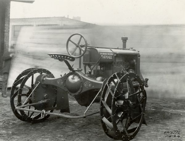 Rear view of a McCormick-Deering Farmall Regular tractor showing details, including decals. A man in the background is holding a sheet or banner in front of the tractor.