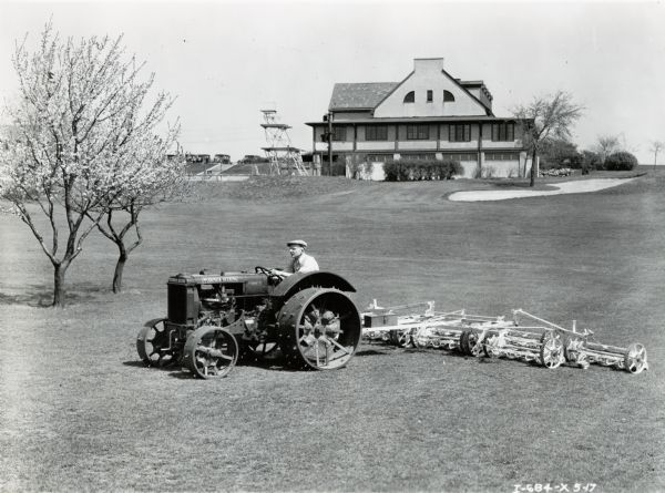 Man mowing a golf course with a Fairway 12 tractor and mower. The club house is in the background.