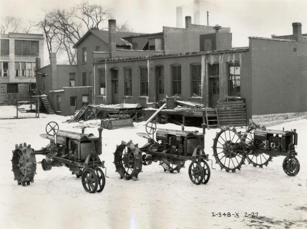Farmall F-30, F-20 and F-12 tractors in a snow-covered yard near a building.