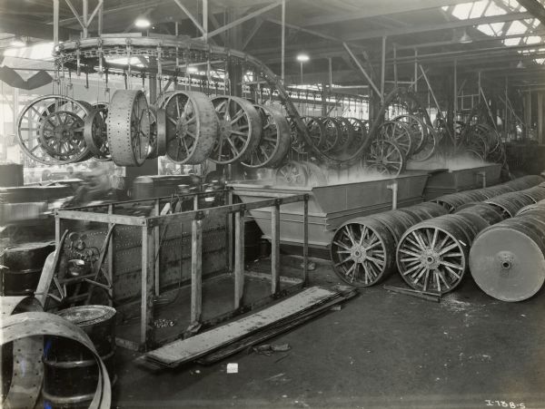 Tractor wheels on an overhead conveyor moving in and out of steaming baths at an International Harvester factory (either Tractor Works or Farmall Works).
