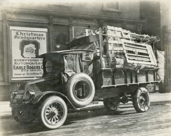 An International G-61 truck parked on an ice-covered city street and loaded with crates. The truck was owned by the G.H. Miller Transfer and Storage Company. A sign on a wall behind the truck reads: "Christmas Headquarters; everything [for] automobiles; Earle Rogers . . .".