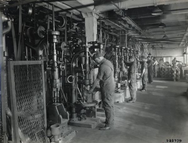 A line of men operate machines at International Harvester's Milwaukee Works (factory).