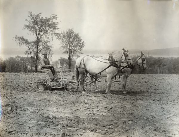 Right side view of a man using a horse-drawn Deering disk harrow in a field.