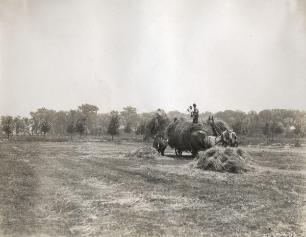 Three men on the ground lift a large pile of hay to two men on a wagon drawn by two horses.