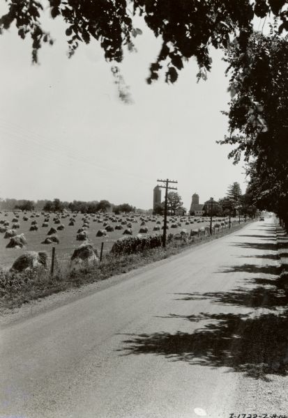 Farm and field near a rural tree-lined road. Cars and trucks can be seen in the distance.