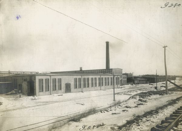 Exterior view of the St. Paul Flax Twine MIll with a railroad track and power lines in the foreground.