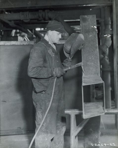 A welder wearing overalls holding a protective mask in front of his face while working at Hawkins Mine.