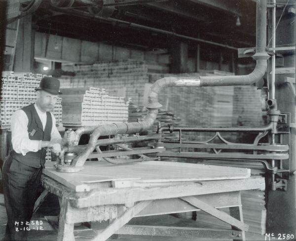 Factory worker(?) sanding a reaper platform at International Harvester's McCormick Works. The man is wearing a bowler hat.