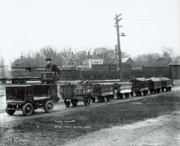 Factory working demonstrating the "new way" of hauling by pulling carts loaded with 16,000 pounds of parts using a shop mule. The man is most likely a worker at International Harvester's Osborne Works (later known as "Auburn Works"). The shop mule was manufactured by the Automatic Transmission Company of Buffalo, New York.