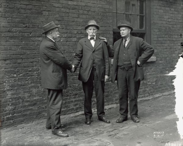 Three older International Harvester employees(?), possibly recent retirees, standing near a brick building. The building may be part of the McCormick Works factory.