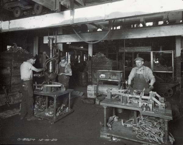 Three factory workers stand at machines at International Harvester's Osborne Works, later known as Auburn Works.