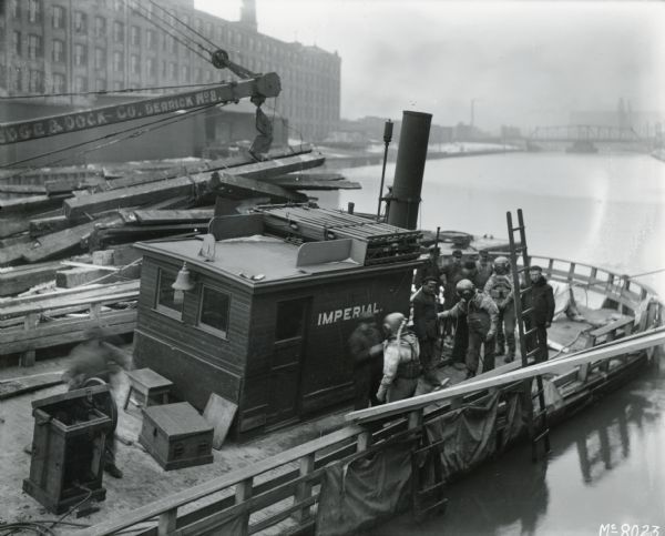 A group of men assisting three men in diving gear on a boat on the Chicago River near the McCormick Works (factory).