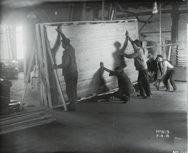 A group of factory workers lift and move a large wooden crate at International Harvester's McCormick Works.