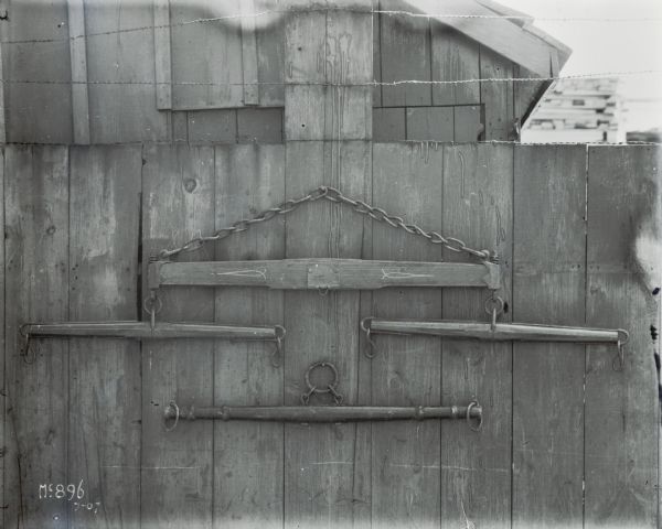 A wooden evener for horse-drawn farm equipment hanging on a wooden, plank fence outside of McCormick Works(?).